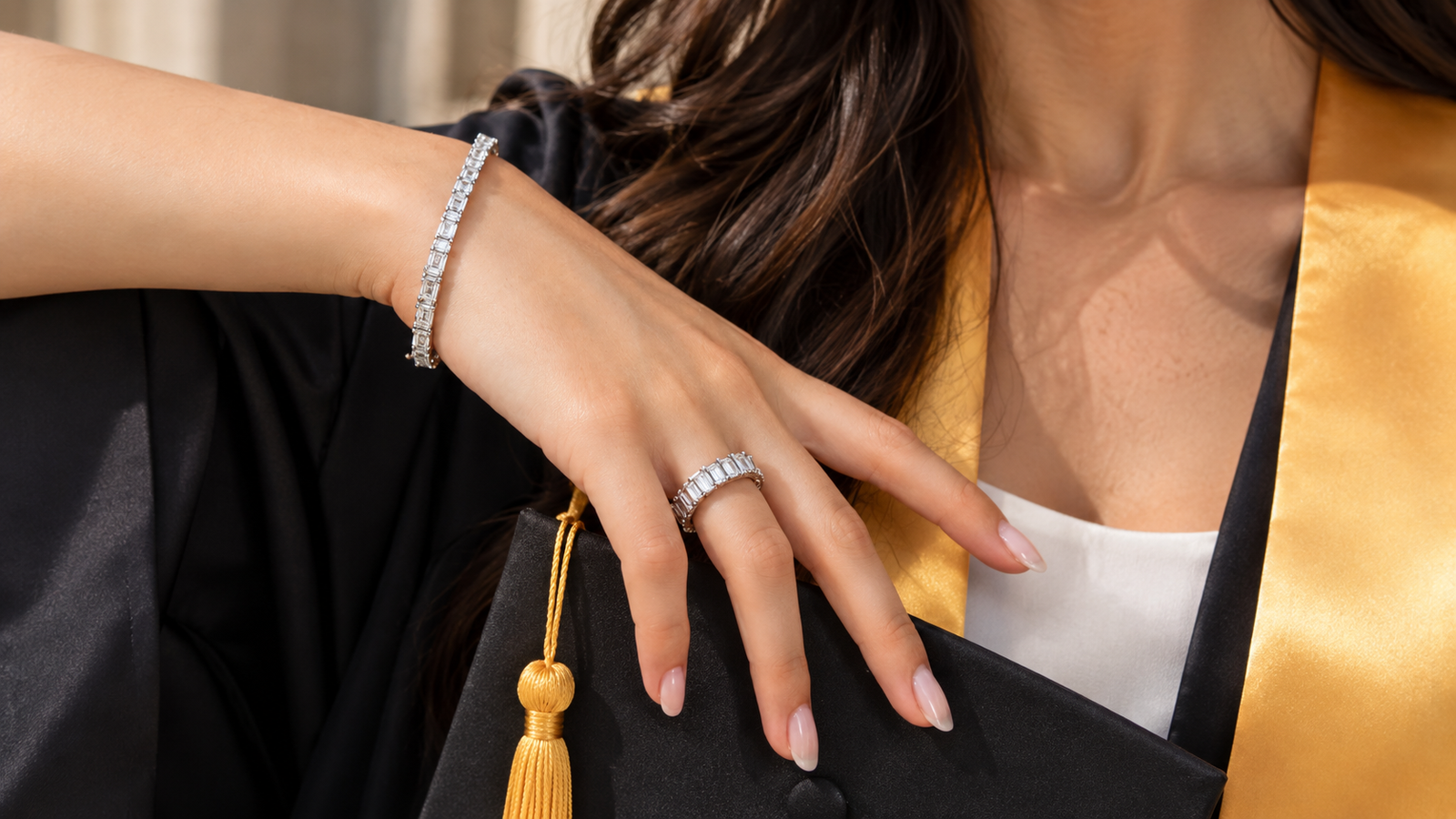 Woman wearing a graduation uniform with a tennis bracelet, tennis necklace, and diamond earrings, showcasing affordable luxury jewelry.
