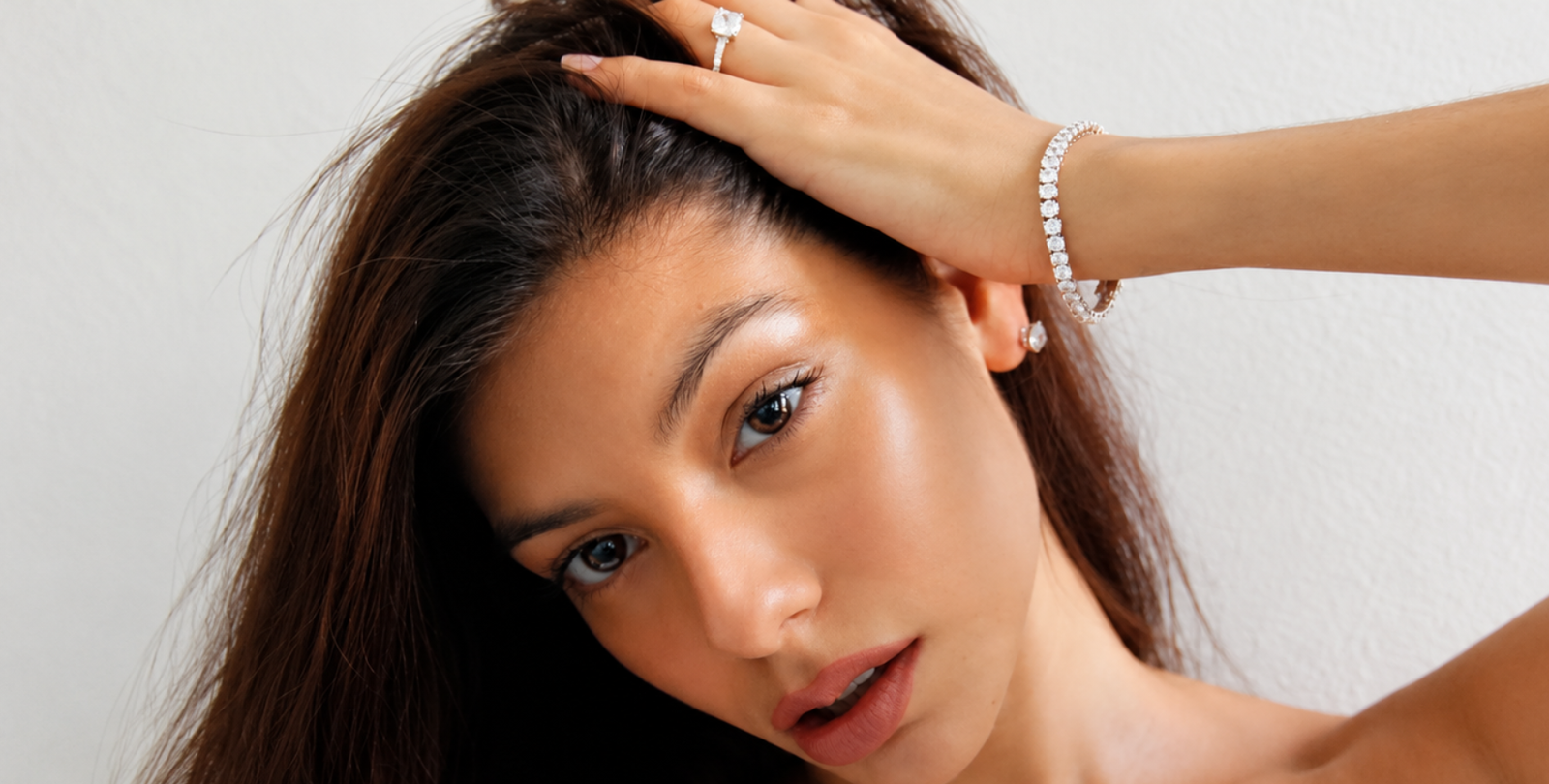 Woman posing with her hand on her head, showcasing a sparkling tennis bracelet as affordable luxury jewelry.