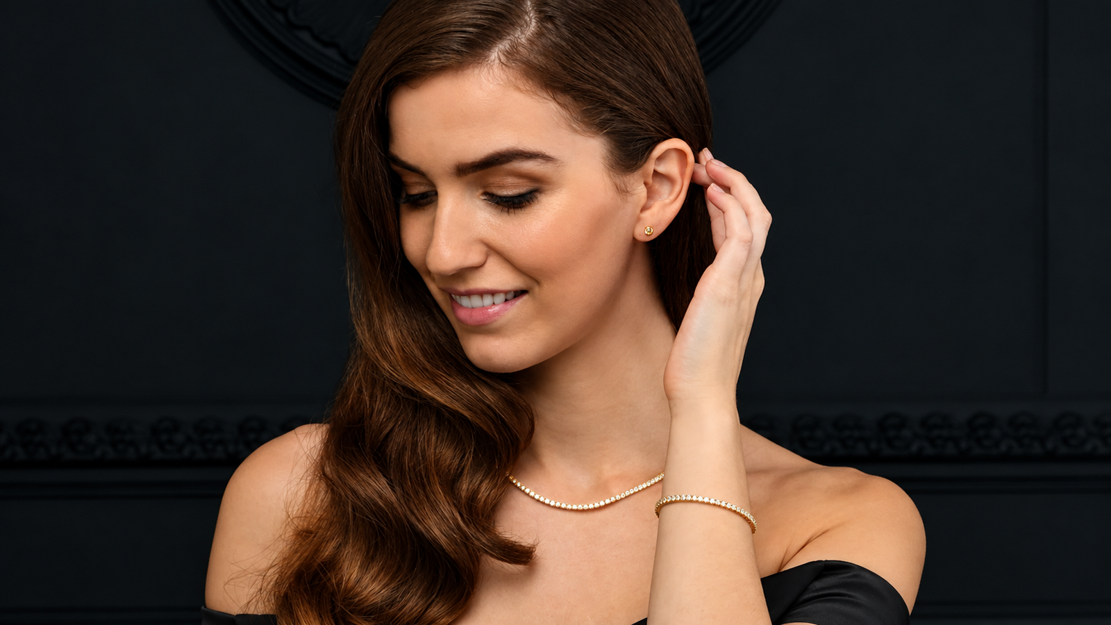 Woman touching the back of her ears, showcasing a tennis bracelet, tennis necklace, and diamond stud earrings as affordable luxury jewelry.